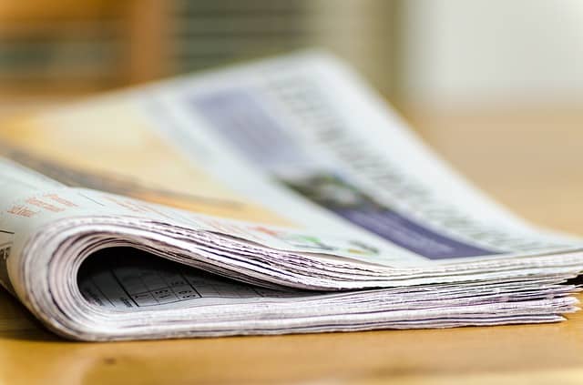 A newspaper is sitting on a wooden table.
