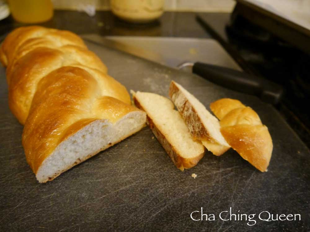 A freshly baked challah bread loaf placed on a wooden cutting board.