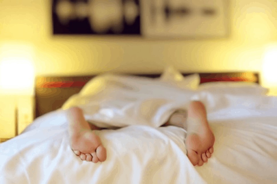 A person's feet are laying in a bed with white sheets.