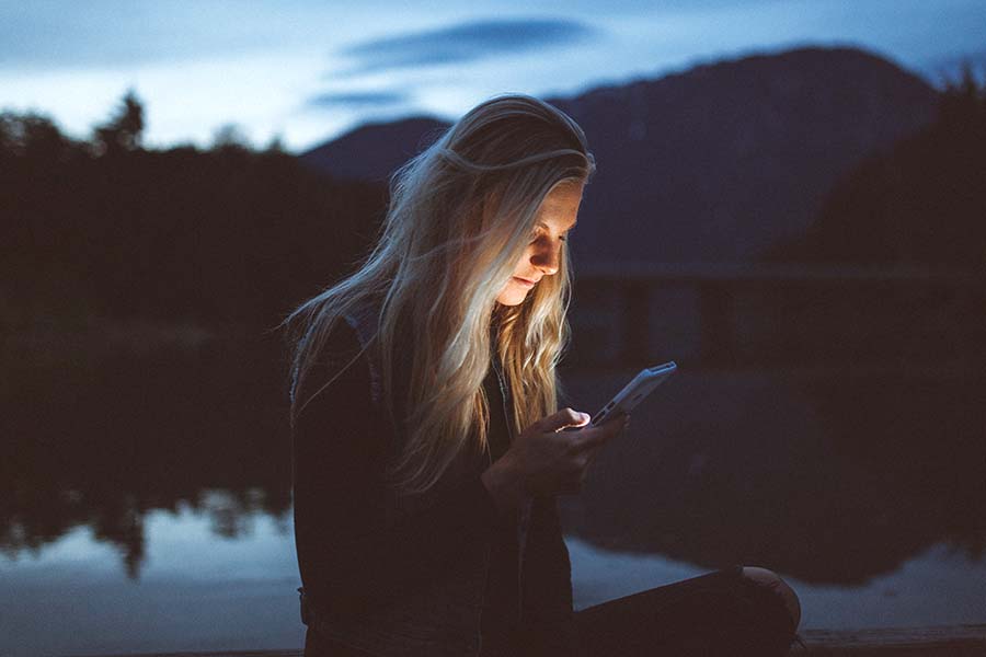 A woman checking her social media on her phone near a lake.