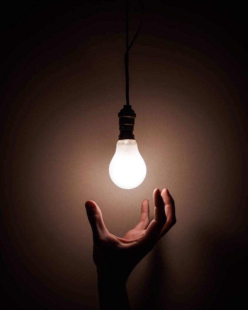 A hand reaching for a light bulb.