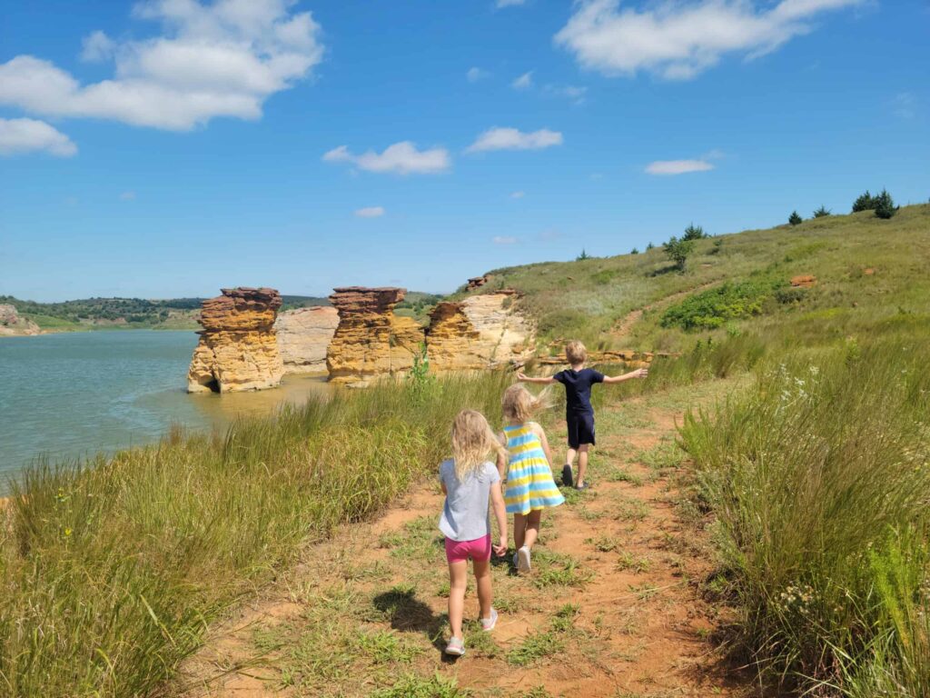 Three children walking along a trail near a lake, enjoying things to do in Kansas.