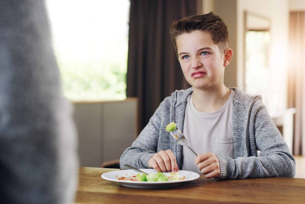 A boy is eating a plate of food with a fork, enjoying the taste of healthy foods.