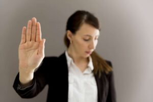 A woman in business attire raises her hand with her palm facing outward as if signaling to stop. She is looking down and away from her hand, perhaps contemplating the high paying jobs people don't want to do.