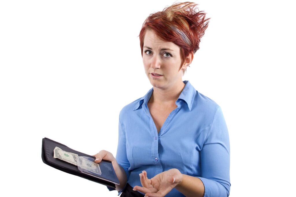 A woman with red hair, wearing a blue shirt, holds an open wallet with cash and gesturing with her other hand, expressing confusion, possibly pondering a nice way to say no tips on credit card transactions.