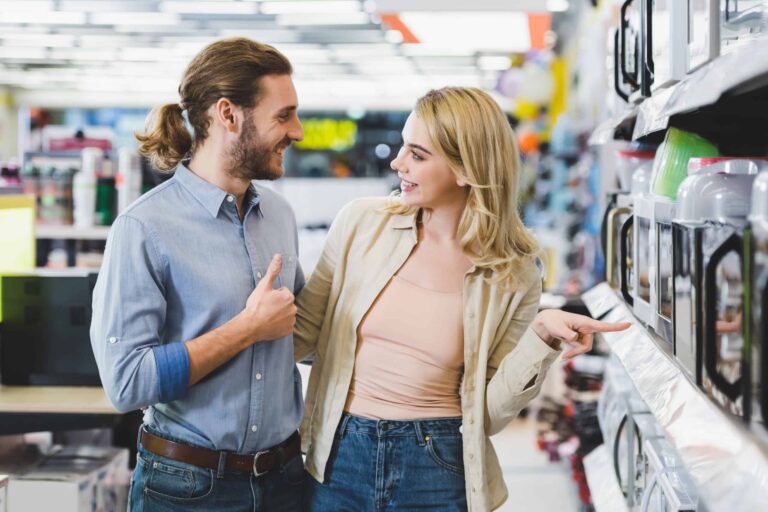 A man and woman smile and talk while shopping for appliances in a store, discussing 10 products that pay for themselves.