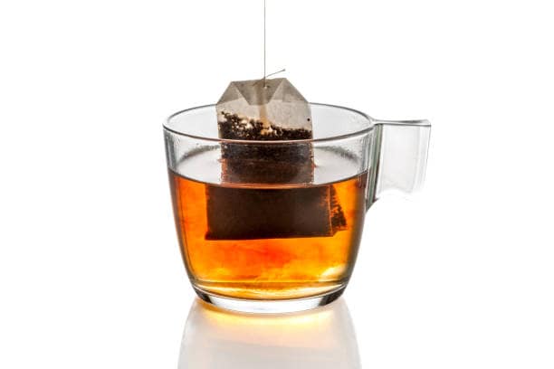 A tea bag is being steeped in a glass cup filled with tea on a white background.