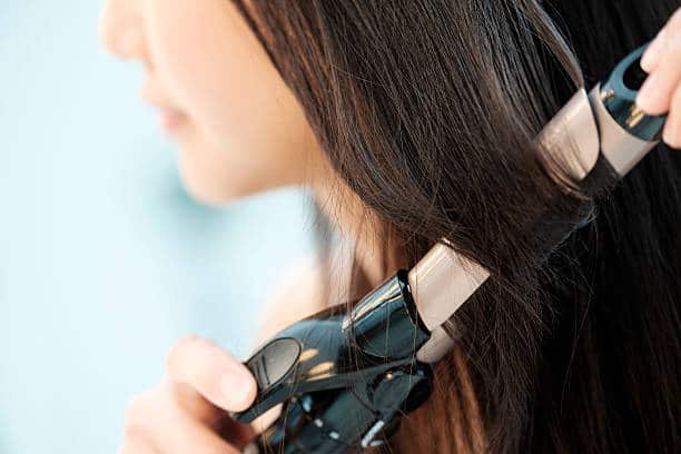 A close-up of a person using a curling iron to curl their long, straight hair.