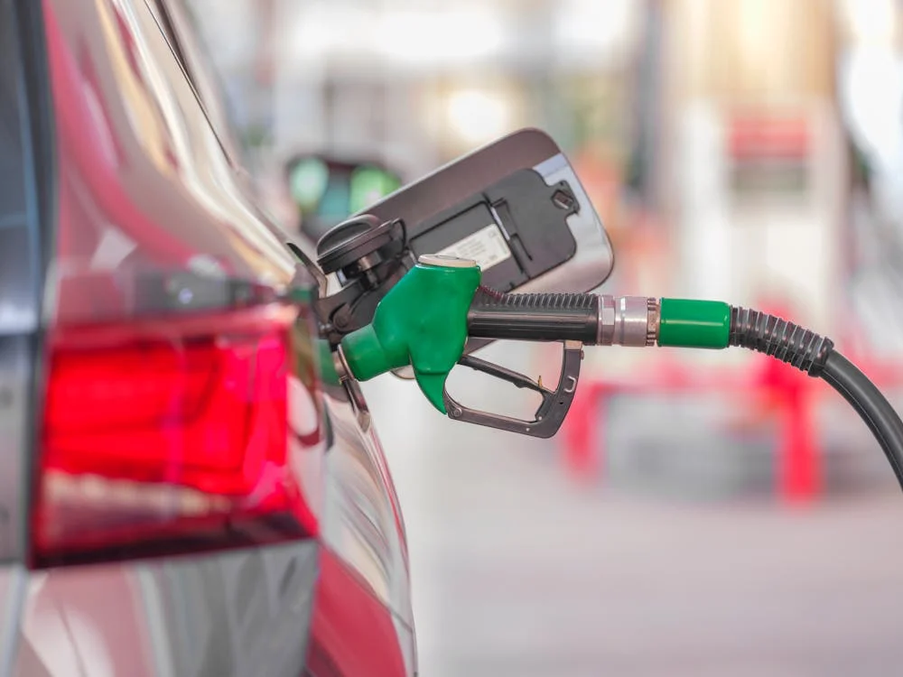 A close-up view of a red car being refueled at a gas station, with a green fuel nozzle inserted into the fuel tank—a place not to tip.