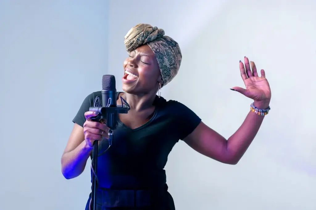 A woman wearing a headwrap sings passionately into a microphone with one hand raised, set against a neutral background reminiscent of places where it is not recommended to leave a tip.