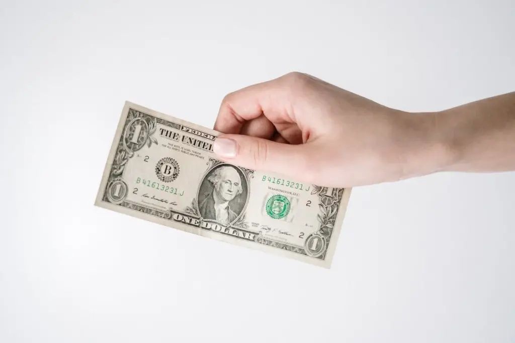 A hand holding a one-dollar bill with the portrait of George Washington facing forward, highlighting how Americans are tired of tipping.