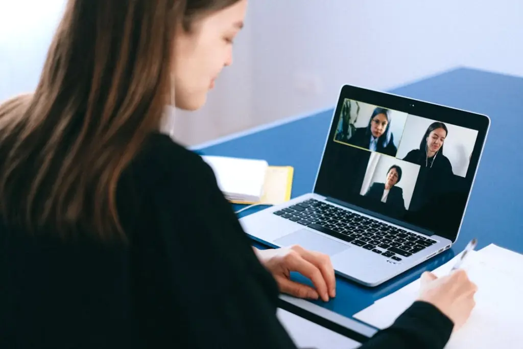 A person is sitting at a desk, participating in a video conference on a laptop with four other people visible on the screen—one of many things replaced by technology in today's interconnected world.