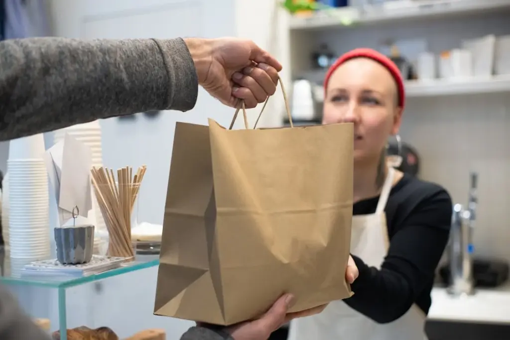 A person in an apron hands a brown paper bag to another person across a counter in a store, one of those places where it is not recommended to leave a tip.