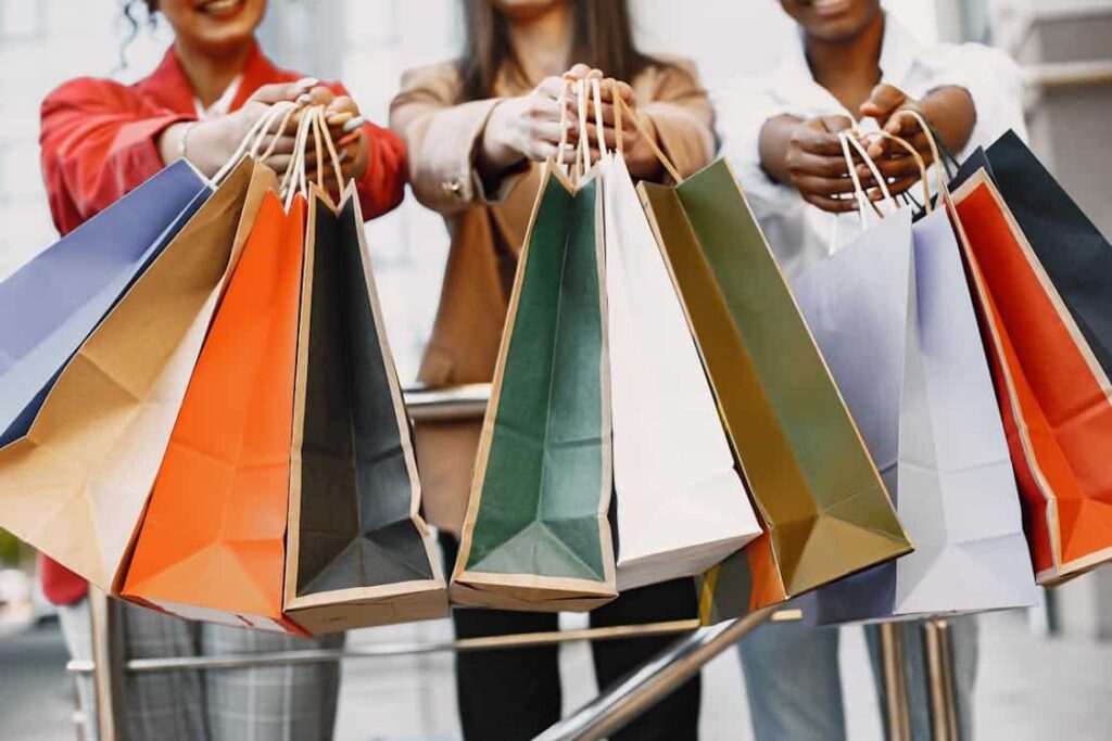 Three people holding multiple colorful shopping bags in an outdoor setting.