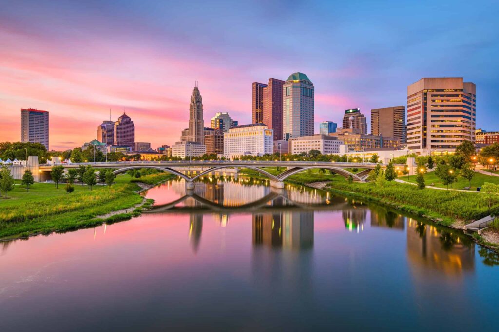 View of downtown Columbus, Ohio, skyline at twilight, with the Scioto River and bridges in the foreground and a colorful sky in the background—an inviting scene in one of the most comfortable places to live in the US.