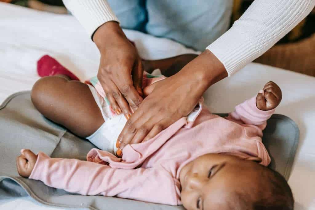 An adult is changing the diaper of a baby lying on a changing mat, dressed in a pink outfit. Using cloth diapers, which are better for diaper rash, ensures the baby stays comfortable and dry.