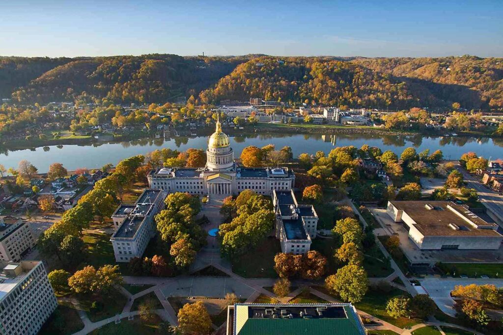 Aerial view of a capitol building with a gold dome surrounded by trees and buildings, near a river and hills in the background under a clear blue sky, showcasing one of the most comfortable cities to live in the US.