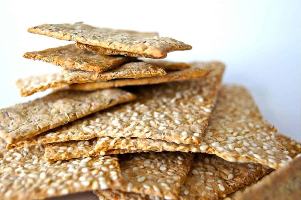 A close-up image of a stack of sesame seed crispbread crackers against a plain white background.