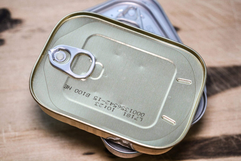Two stacked rectangular metal cans with pull-tab lids and printed codes on a wooden surface.