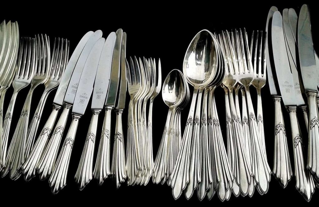 A set of silverware including forks, knives, and spoons is arranged against a black background.