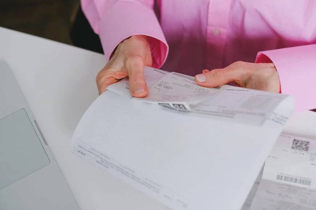 Person in pink shirt holding and organizing receipts at a desk.