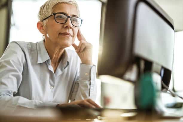 An older woman with short gray hair and glasses intently working on a computer.