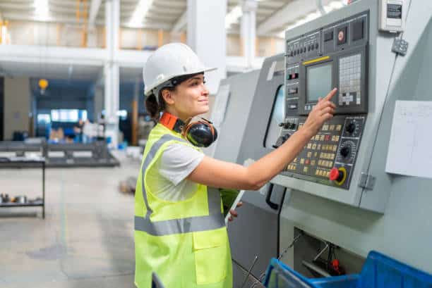 A person in a high-visibility vest and white helmet operates a control panel in an industrial setting.