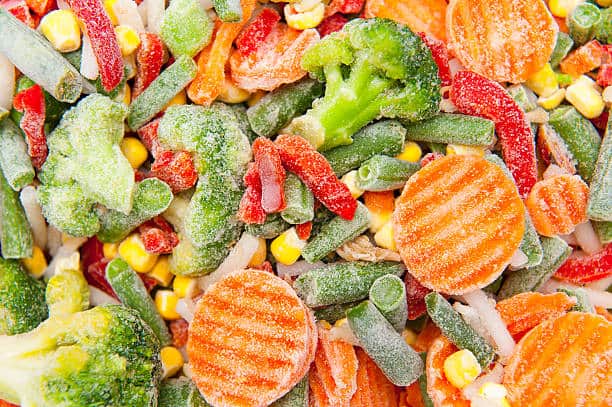 A close-up of assorted frozen vegetables, including broccoli, sliced carrots, green beans, red bell peppers, and corn.