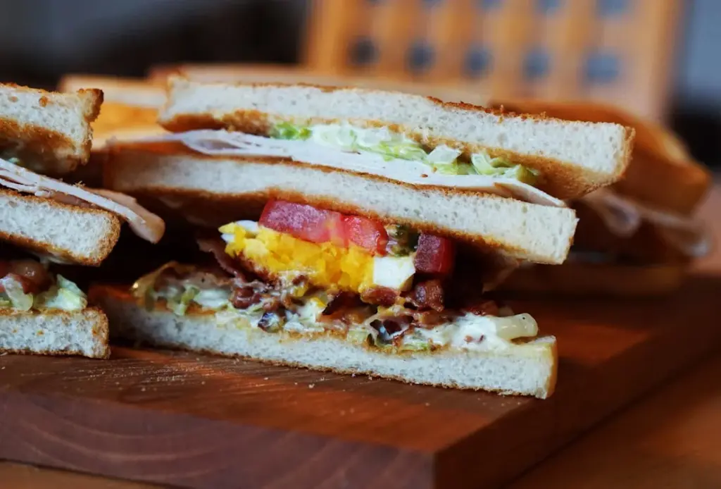 Close-up of a club sandwich cut into quarters, showing layers of bread, lettuce, tomato, bacon, a fried egg, and meats.