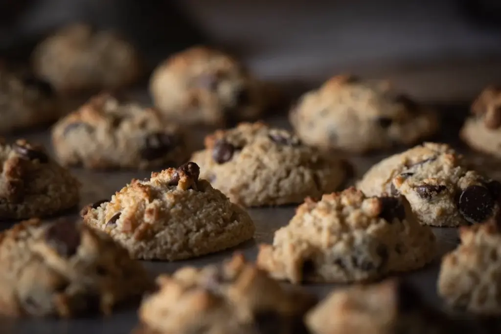 Close-up of several freshly baked chocolate chip cookies on a baking tray. The cookies are golden brown and slightly crispy around the edges.