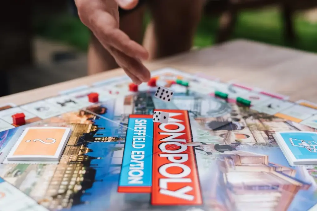 A hand is rolling dice over a Monopoly board labeled "Sheffield Edition," with various game pieces and cards visible on the board.