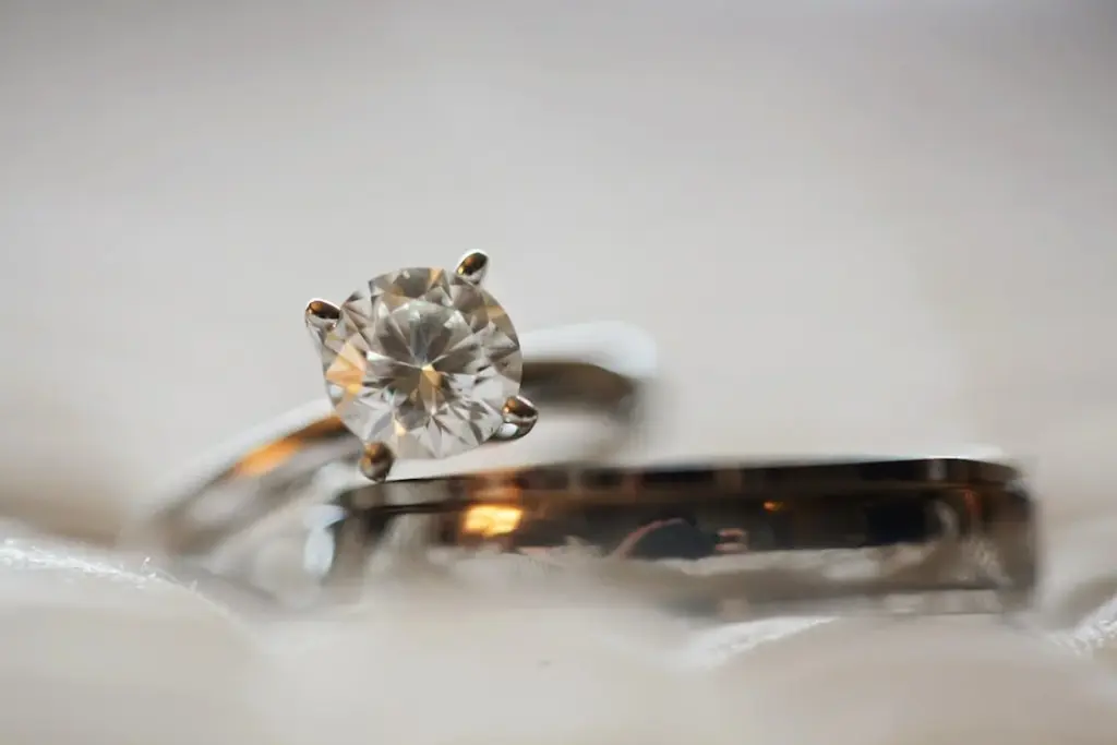 Close-up of a diamond ring with a round cut stone set in a prong setting, placed next to a plain metal band.