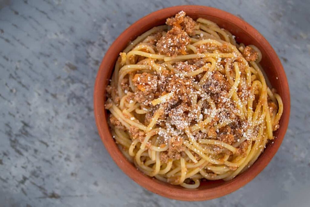 A bowl of spaghetti with meat sauce topped with grated cheese.