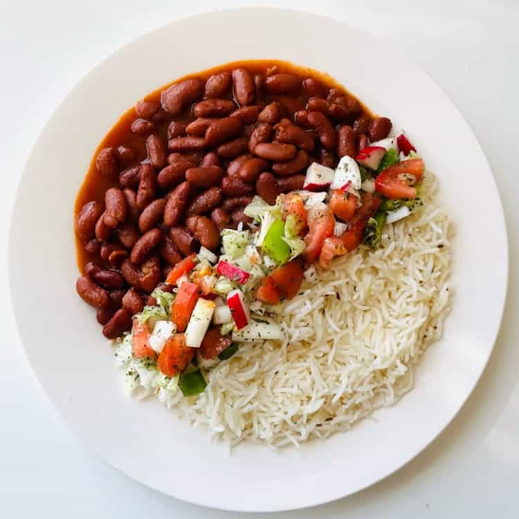 A plate of white rice, kidney beans in sauce, and a vegetable salad with tomatoes, cucumbers, and feta cheese.