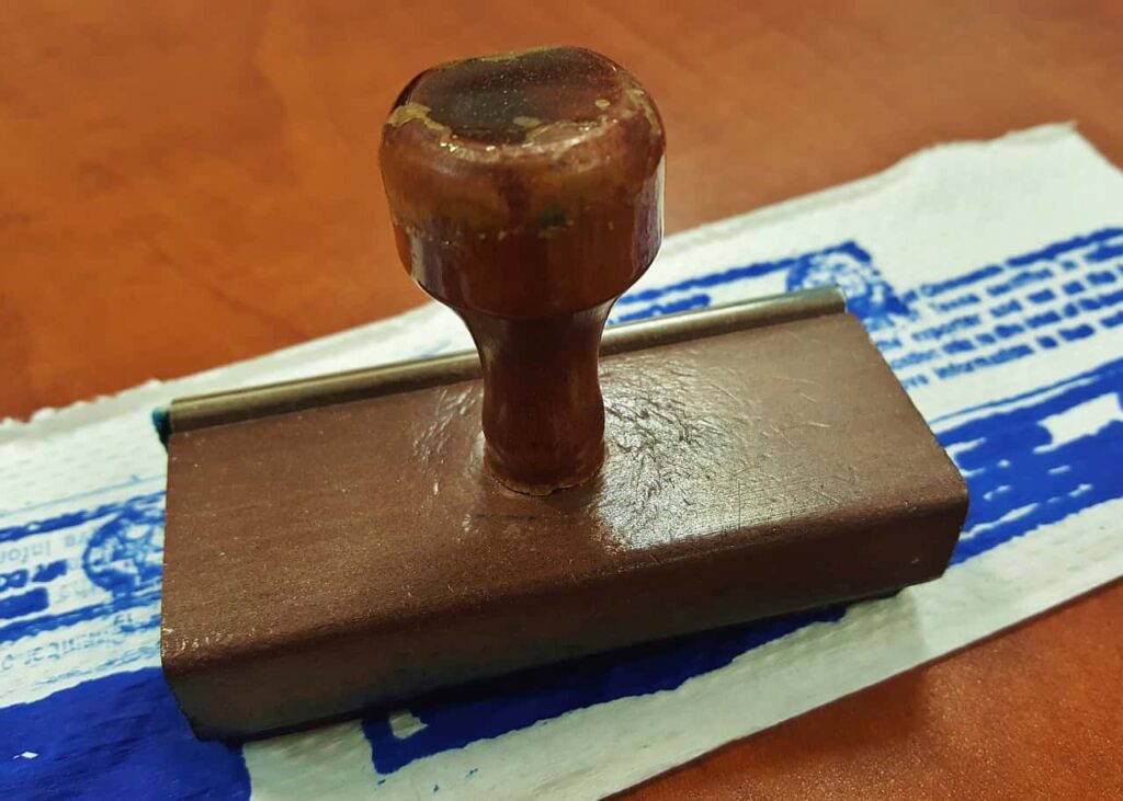 A wooden stamp with a raised handle is placed on a piece of paper that has blue ink marks.