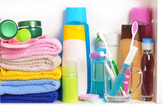 A shelf containing folded colorful towels, various bottles of toiletries, a clear cup holding toothbrushes, and small containers of personal hygiene products.