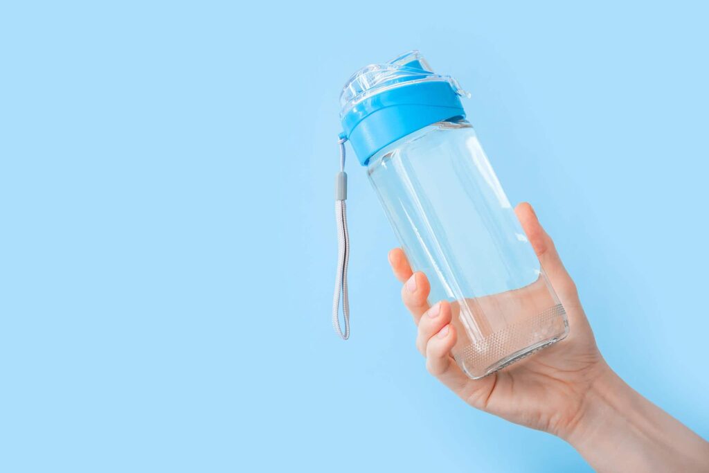 Hand holding a clear water bottle with a blue lid and a carrying strap, against a light blue background.