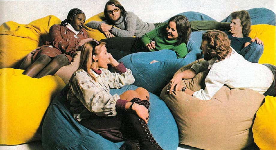 A group of six people is sitting and relaxing on colorful bean bags, engaged in conversation. The background is plain and white.