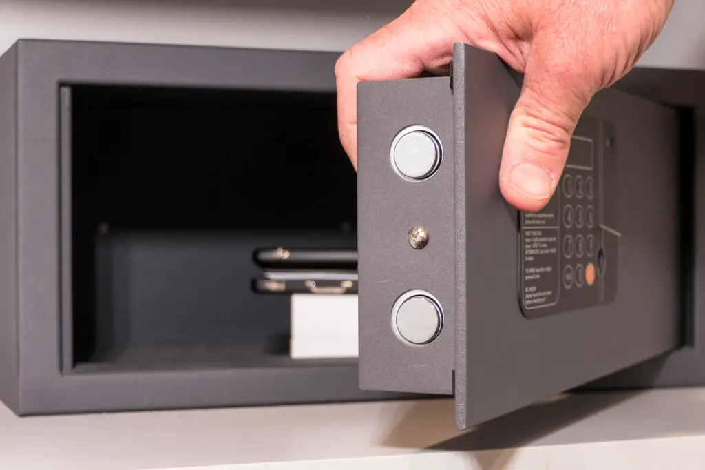 A person opens a safe containing two mobile phones and a small white box.