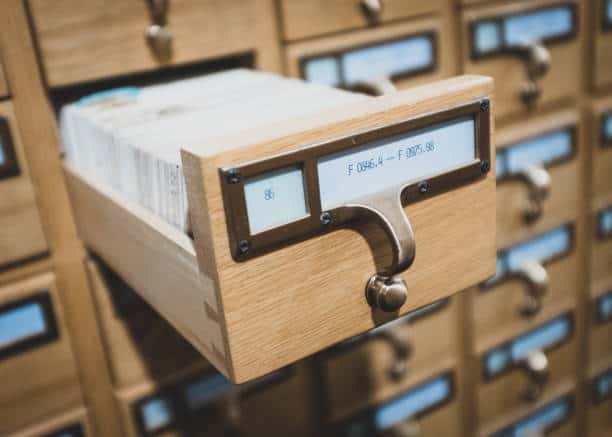 A wooden library card catalog with one drawer open, revealing index cards inside.