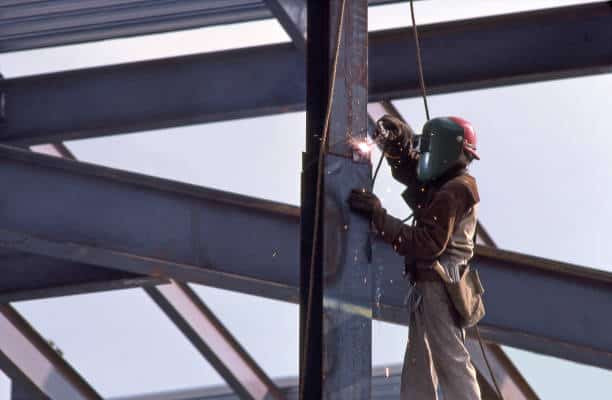 A construction worker wearing protective gear uses a welding tool on a steel framework at a building site.