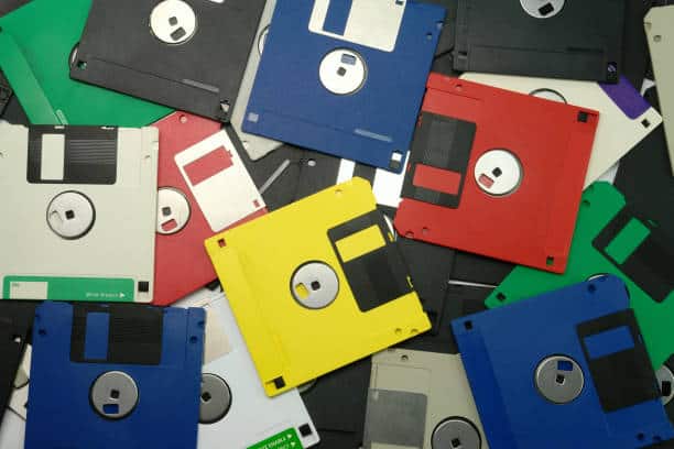 A scattered collection of colorful 3.5-inch floppy disks, including blue, yellow, red, green, black, and white, on a flat surface.