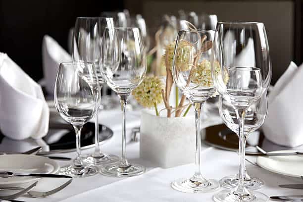 A formal dining table set with white napkins, wine glasses, and a centerpiece of flowers in a white vase.