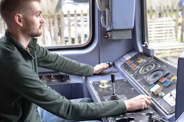 A person operating a train by sitting in the driver's cabin, handling various control mechanisms.