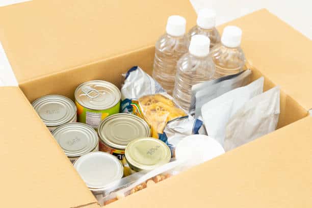 A cardboard box containing multiple cans of food, three bottled waters, and various food packets.