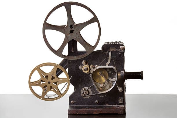 Vintage film projector with two reels and visible internal mechanisms, set against a white background.