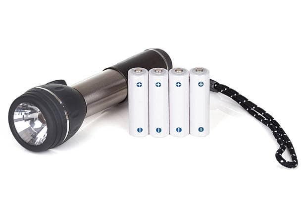 A black and silver flashlight is placed next to five white AA batteries in a single line. The flashlight has a wrist strap attached.