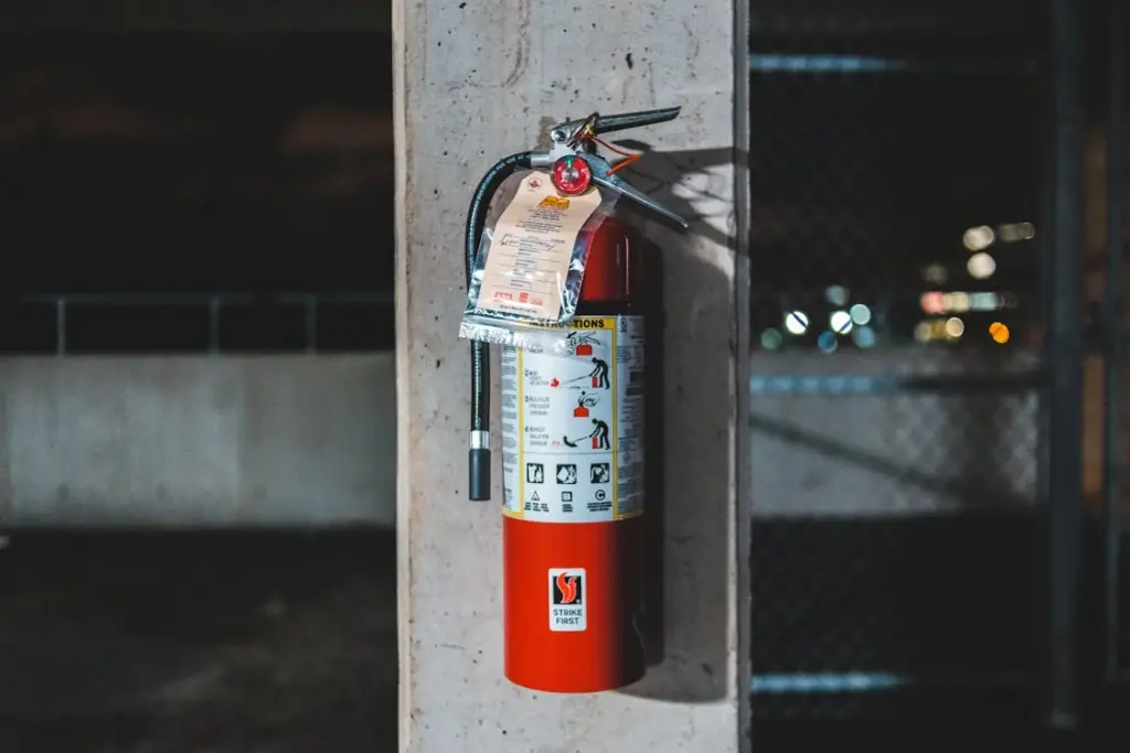 A red fire extinguisher mounted on a concrete wall in an industrial setting, with an inspection tag attached to the top.