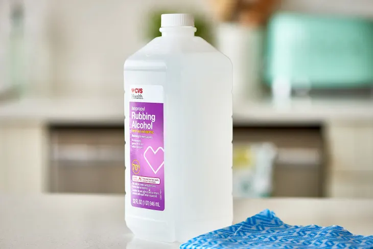 A bottle of CVS Health Isopropyl Rubbing Alcohol is placed on a countertop next to a blue patterned cloth.