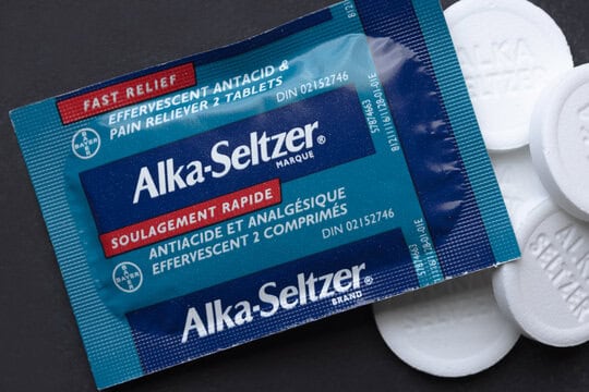 A packet of Alka-Seltzer tablets, labeled as providing fast relief for antacid and pain. Some white tablets are visible next to the packet.